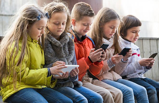 ordinary kids sitting with mobile devices in street